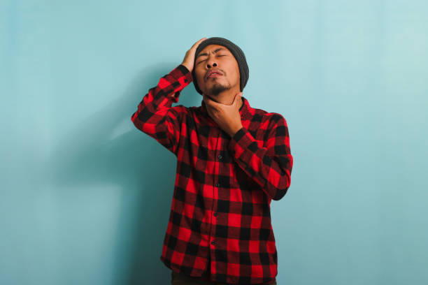 istock Young Asian man suffers from headache and sore throat while standing against a blue background 1567934428