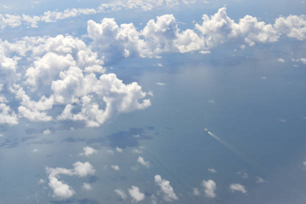 Viewed from high altitude throughout white clouds floating above coats with a small boat running on the sea.