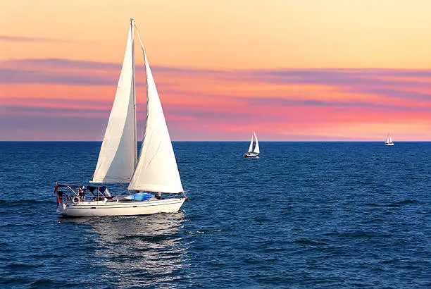 Sailboat sailing towards sunset on a calm evening