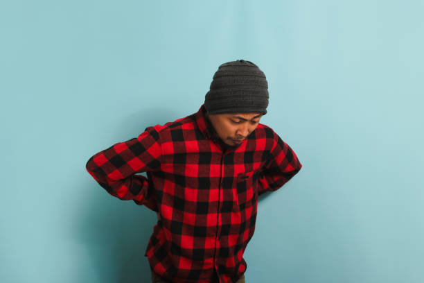 istock Young Asian man is suffering from a backache, experiencing back pain, isolated on a blue background 1567978183