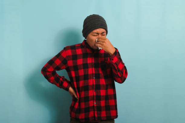 istock Young Asian man is sneezing into tissue, suffering from cough, and flu, isolated on blue background 1567978187