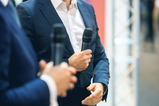 Midsection of two unrecognizable businessmen holding a microphone and discussing at a public event