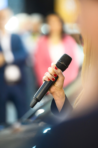 A woman in the audience, a journalist or a participant, holds a microphone and asks a question or speaks at a rally, copy space