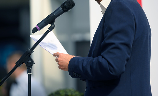 Public speaker stands behind a microphone and makes a statement at a public event or press conference