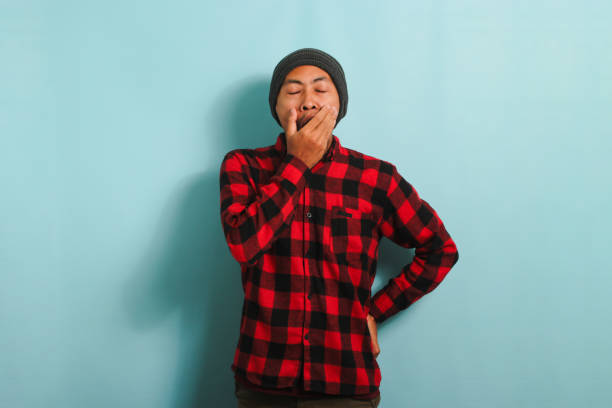 istock Tired young Asian man yawns feeling exhausted due to overwork insomnia, isolated on blue background 1567996176