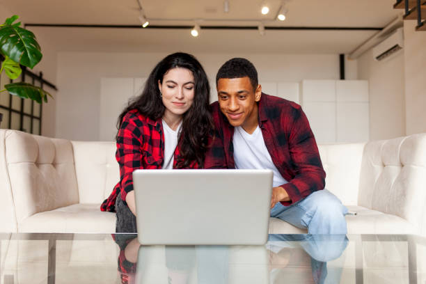 istock young multiracial couple sitting on comfortable sofa and looking into laptop at home 1568002196