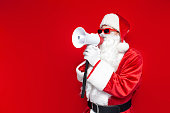 santa claus in red glasses announces information into megaphone on colored background