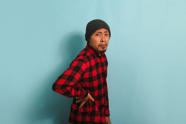 istock Young Asian man is suffering from a backache, experiencing back pain, isolated on a blue background 1568014079