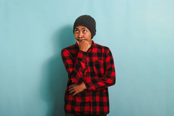 istock Thoughtful Young Asian man holds his chin, making plans, isolated on a blue background 1568019404