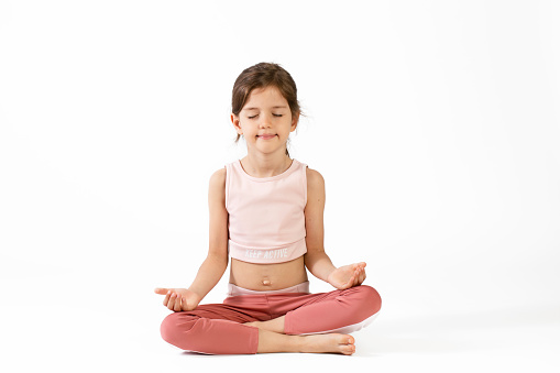 Cute girl doing yoga exercise in front of white background.