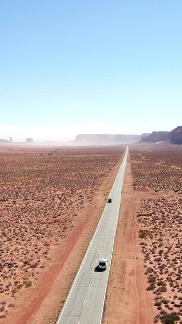 A Tracking Vertical Drone Shot of a Conversion Camper Van Driving On Oljato Road in Monument Valley in on a Sunny Clear Sky Day