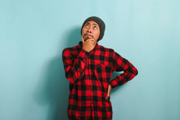 istock Thoughtful Young Asian man holds his chin, making plans, isolated on a blue background 1568039583