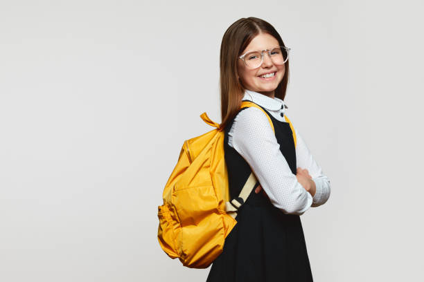 studentessa in occhiali con zaino giallo che tiene le mani incrociate mentre sorride felice, copia lo spazio - schoolgirl school children isolated child foto e immagini stock