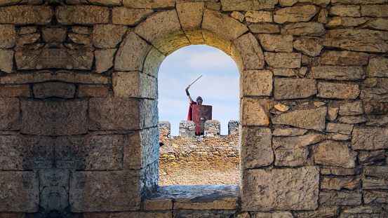 Roman guard raising sword declares victory behind a citadel window.