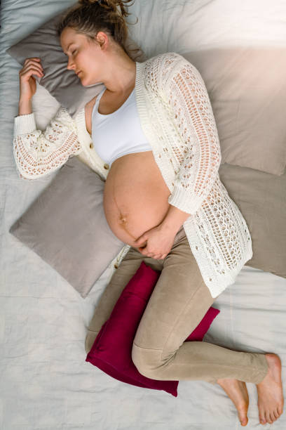 istock Expectant mother sleeping on sofa while gently holding her naked baby belly. Bright shot. 1568163391