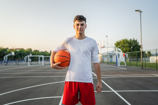 One teenager caucasian male caucasian young man stand on basketball court with ball in the evening ready to play game copy space real person