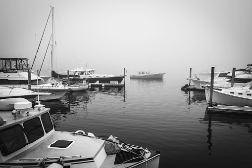 Tranquil foggy summer seascape with moored boats and recreational vessels at Boothbay Harbor Marina in Lincoln County, Maine