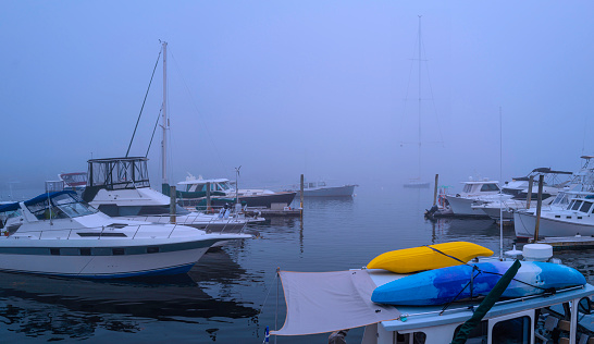 Tranquil foggy summer seascape with moored boats and recreational vessels at Boothbay Harbor Marina in Lincoln County, Maine