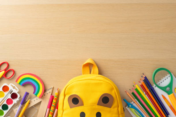 istock Classroom essentials layout. Top view of assorted tools, album, painting set, color pencils, ruler, magnifier, playful bear bag, rainbow plasticine on wooden desk backdrop with room for text 1568181585