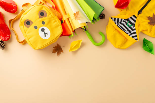 istock Practical waterproof ensemble for kids during rainy days. Capture a top view photo featuring colorful gum boots, a raincoat, backpack and an umbrella on a beige backdrop, perfect for text or ads 1568181765
