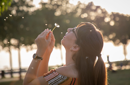 Young woman blowing dandelion in front of lights