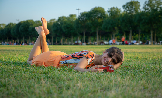 Young colorfully dressed woman lying on the floor in public park dealing with her phone