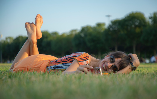 Young colorfully dressed woman lying on the floor in public park dealing with her phone