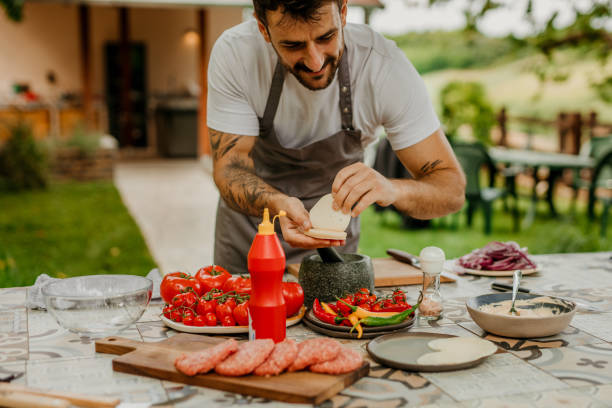 istock Handsome mid aged Man Cooking Delicious BBQ Meal in His Outdoors Summer Kitchen 1568182332
