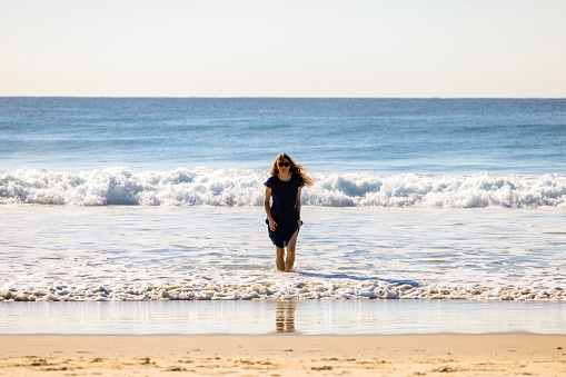 Woman walking from ocean waves near beach and enjoying the beauty of nature, background with copy space, full frame horizontal composition