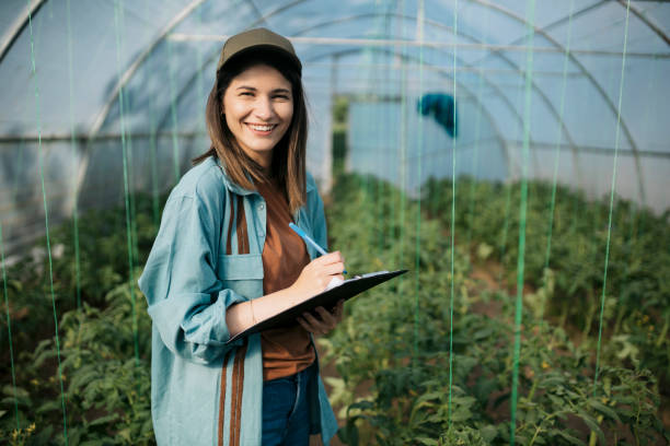Caucasian garden worker writing notes on a clipboard working in a greenhouse stock photo