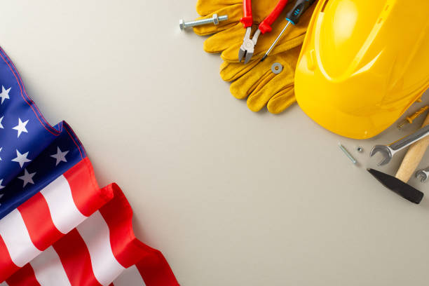 istock Labor Day celebration with construction professionals: top-view shot, featuring a flag, helmet, gloves, and building instruments on grey isolated background. Ideal for Labor Day content 1568184923