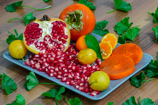 Nashi pear, Pomegranate, Persimmon sliced and whole, Mandarin sliced and whole with leaf, Green plate, Mallow leaf on wooden table