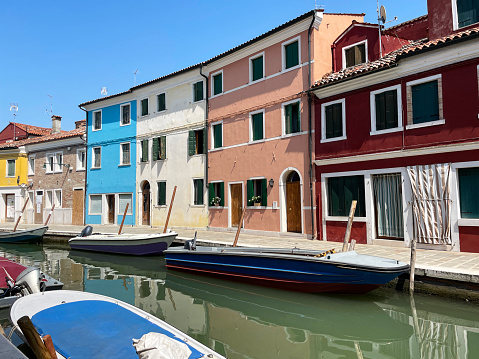 Stock photo showing view of a canal lined with colourful buildings and moored boats in Burano, Venice, Italy. Famous for lace making, Burano is an island in the Venetian Lagoon.