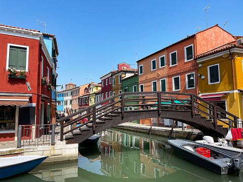 Stock photo showing view of a canal lined with colourful buildings and moored boats in Burano, Venice, Italy. Famous for lace making, Burano is an island in the Venetian Lagoon.
