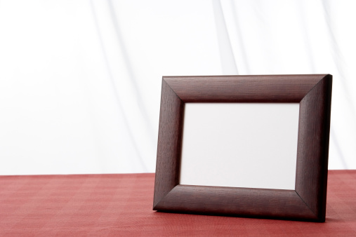 Blank brown wooden picture frame on the table in front of white curtain with copy space.