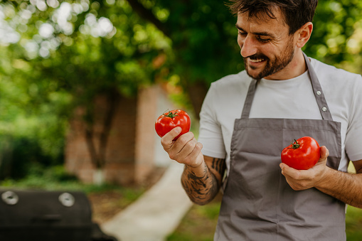 Cheerful male using tomato for salad preparing for an outdoor bbq meal.