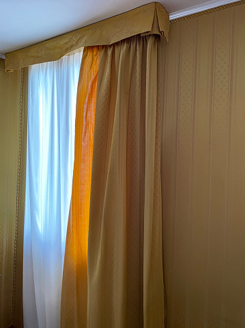 Stock photo showing gold striped curtains hanging at wood frame window with wall papered with matching patterned paper.