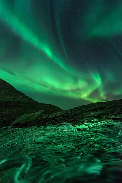 A powerful display of northern lights over a small creek in the alpine regions of Norway.