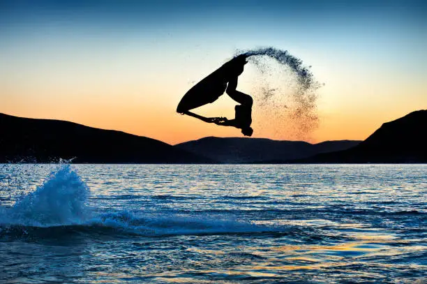 Silhouette of a jet ski rider performing a backflip.