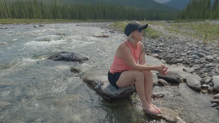 Woman relaxes by river edge, looks off