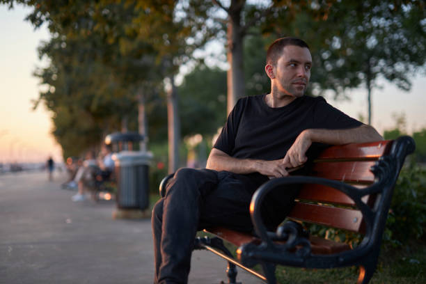 istock handsome young man sitting on a park bench 1568315009