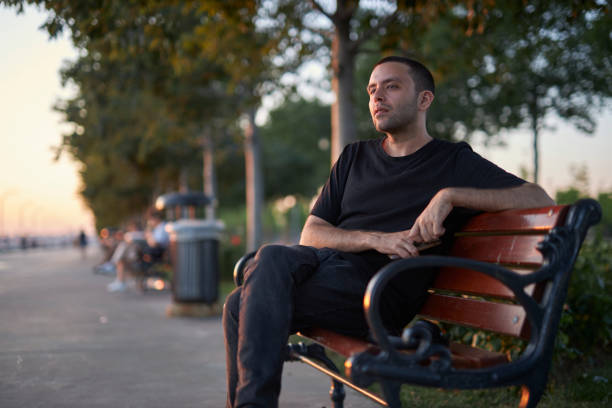 istock handsome young man sitting on a park bench 1568318778
