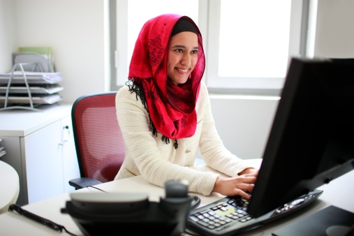 Asian / Malay / Muslim female professional working on computer, smiling.