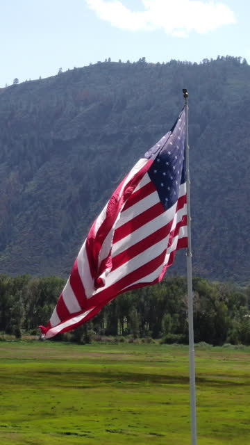Vertical Drone Shot of an American Flag Waving Proud in an Open Field in the Mountains Near Ouray Colorado on a Sunny Day with Lite Clouds in the Sky