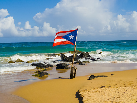 Puerto Rican flag on the Beach in front of ocean waves crashing over the rocks