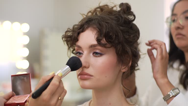 Close-up of unrecognizable wedding makeup artist making fashion make up for beautiful bride in beauty salon. Hairdresser making hairstyle using curling tongs