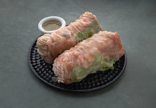 Homemade Riceberry Rice paper Spring rolls stuffed with sliced Chicken and fresh Vegetables served with asian chili sauce on black ceramic plate. Space for text, Selective focus.