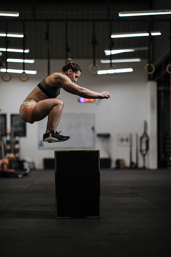 A woman working out alone in a gym jumps on the box