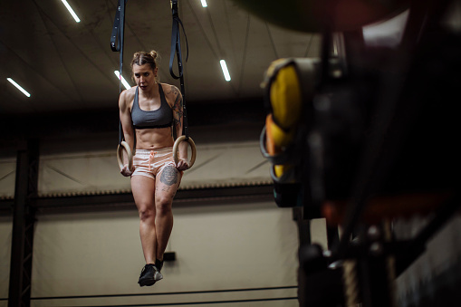 In the gym, a strong young woman works out on rings