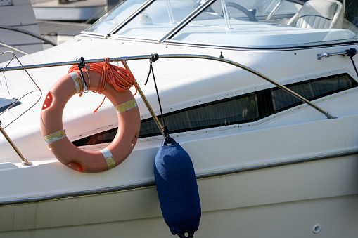 Partial close up of white sport boat in harbor with buoy and life ring belt preserver on railing as concept for protection protect insurance and safeguarding